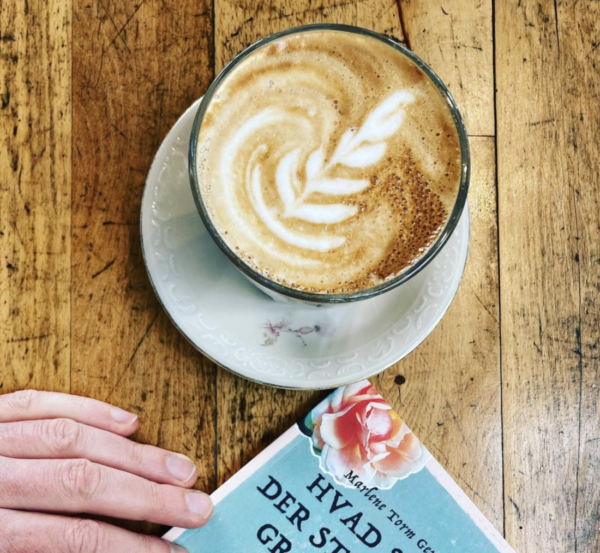 Kaffe med latte-art og bog på et bord.