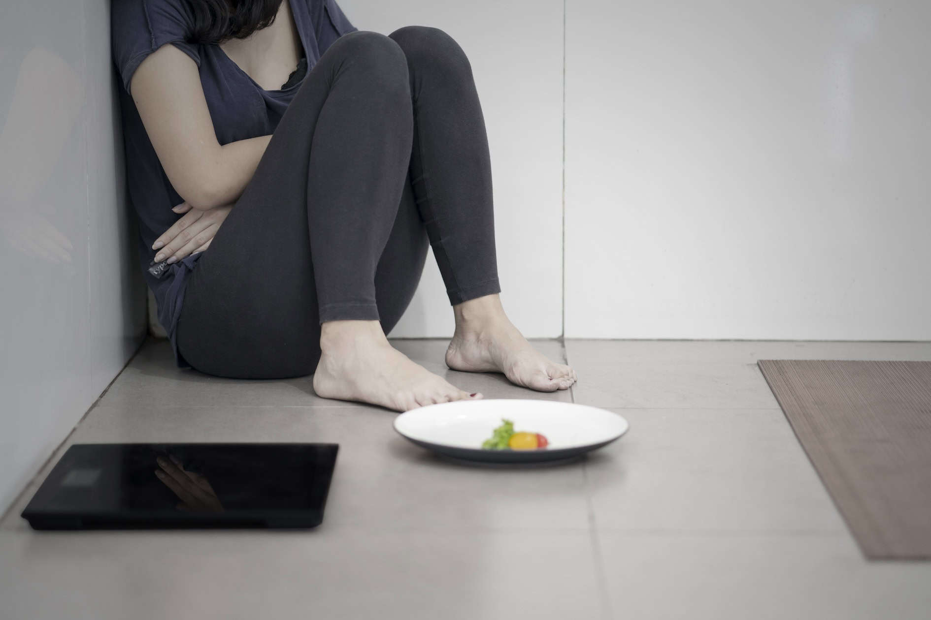 Personne assise au sol avec une assiette vide et une balance, représentant les troubles du comportement alimentaire
