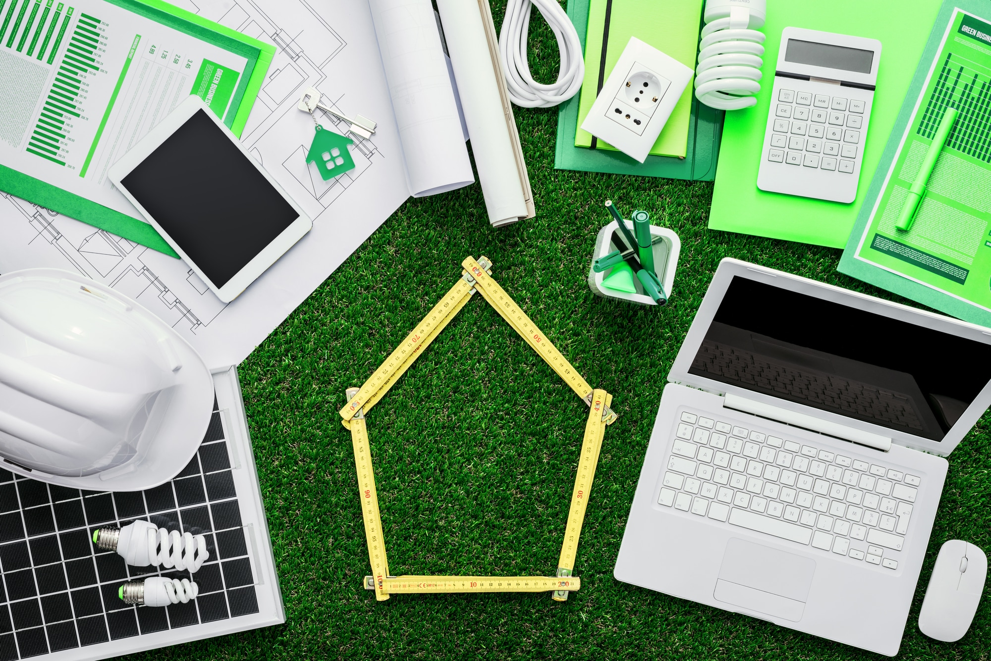 House project, tools, laptop and solar panel on a grass desktop, folding meter composing a house at center, green building concept