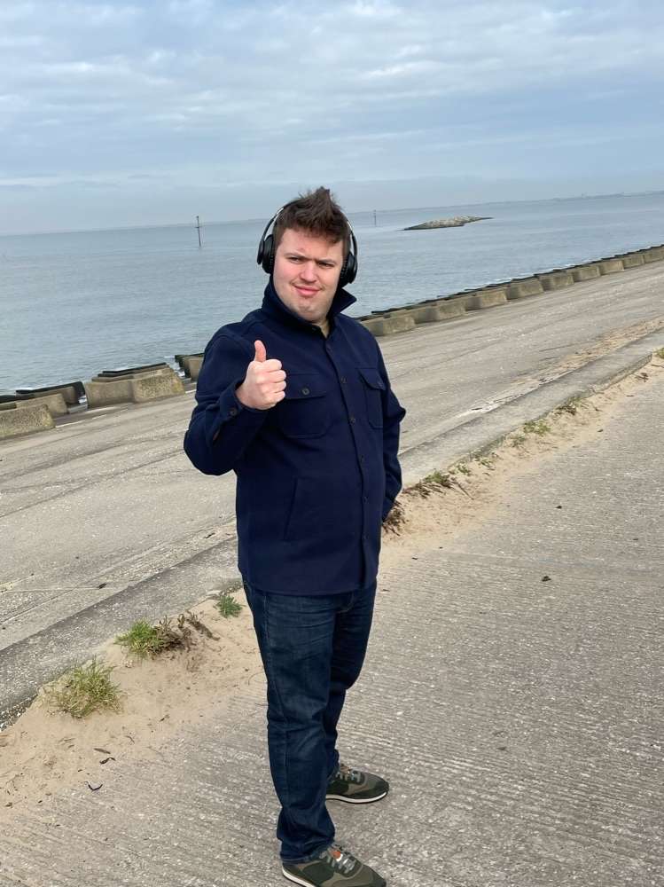 Man wearing headphones gives thumbs up at the beach