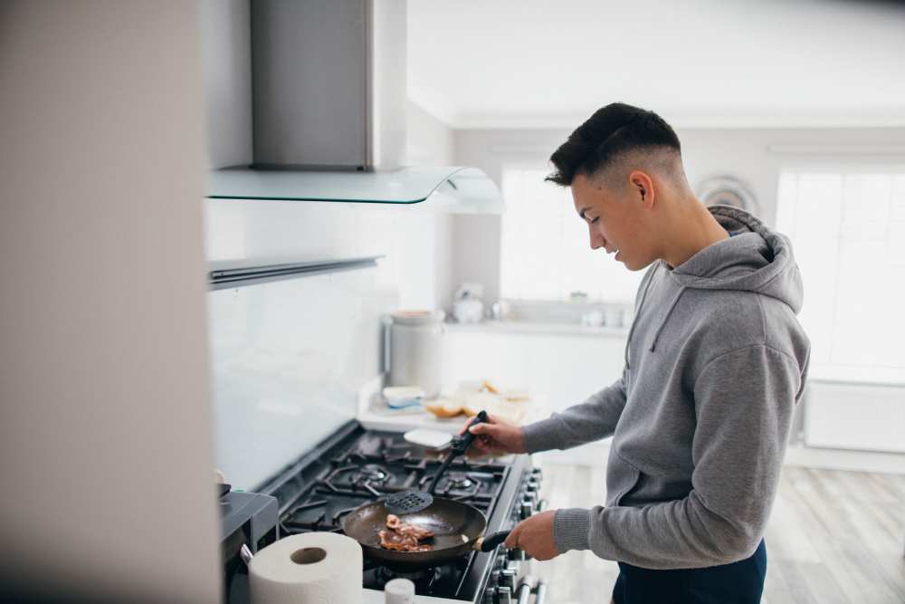 A teenage boy is frying bacon in supported living accommodation