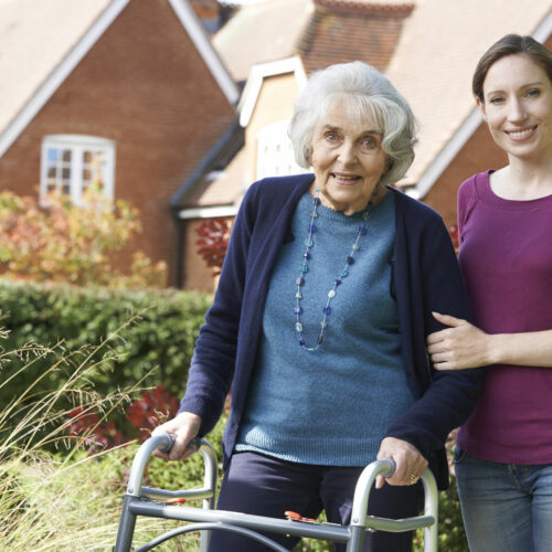 Daughter Helping Senior Mother To Use Walking Frame