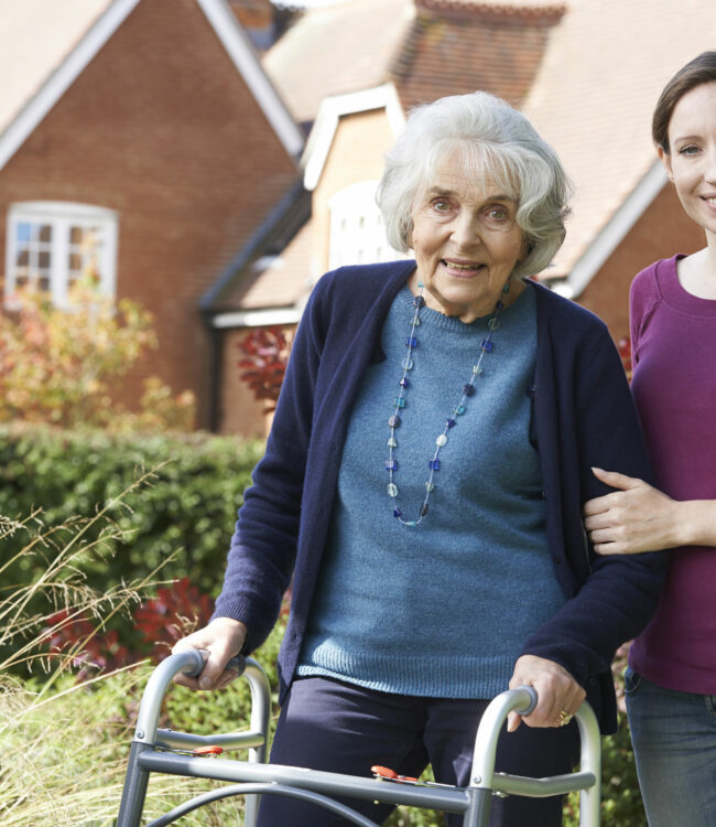 Daughter Helping Senior Mother To Use Walking Frame