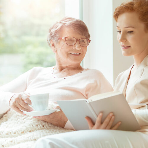 Woman reading a book while sitting with happy grandmother drinking tea