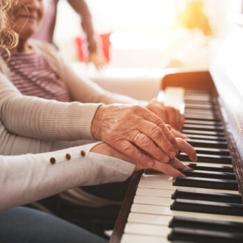 An unrecognizable teenage girl with grandmother playing the piano at home. Family and generations concept.