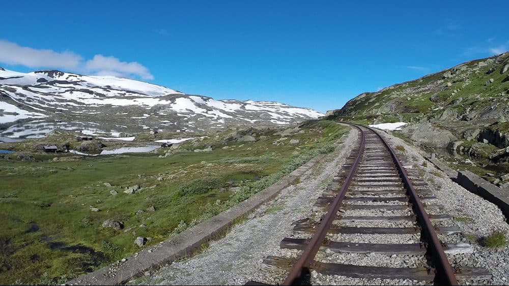 Een treinspoor in het wijdse landschap van Noorwegen met besneeuwde bergen in de verte.