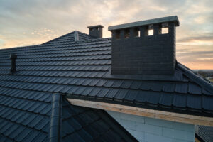 Closeup of brick chimney on house roof top covered with ceramic shingles. Tiled covering of building.