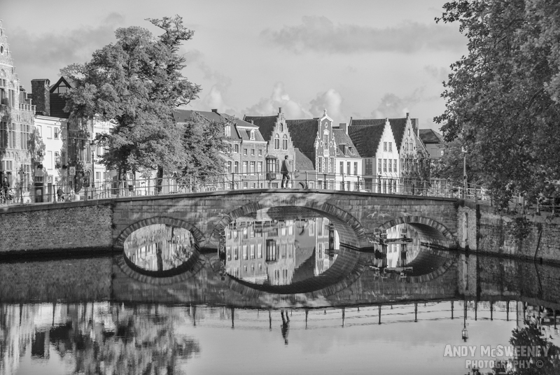 Black and white photo of a bridge over the canal with reflections and gable houses in Brugge, Belgium