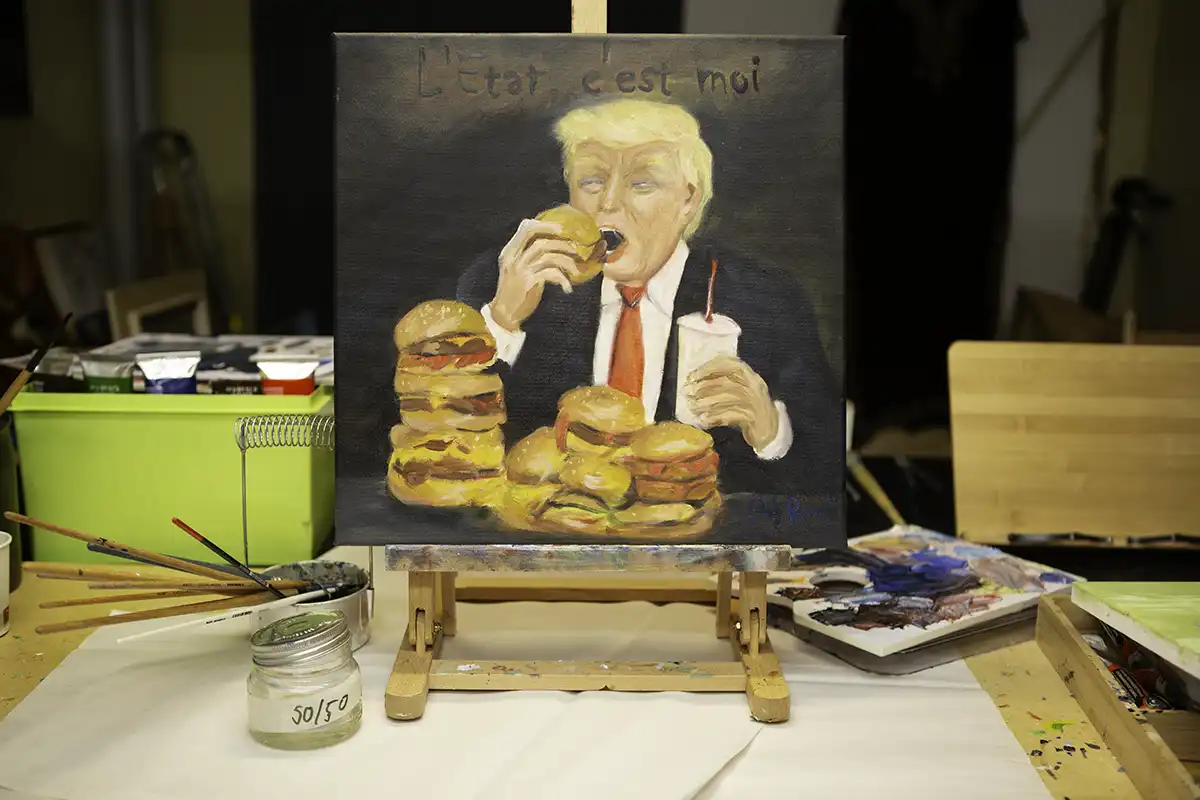 Painting of Donald Trump eating burgers on an easel in an artist studio