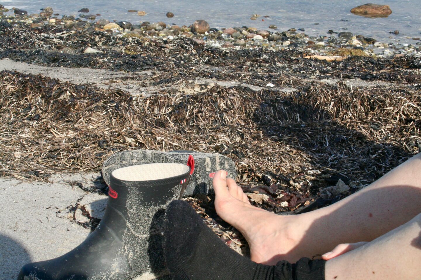 At menneske. At sidde med bare fødder på en tangfyldt strand på Djursland.