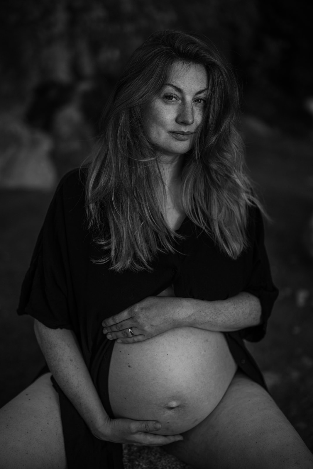 gravid kvinna sitter på en sten och håller händerna på magen