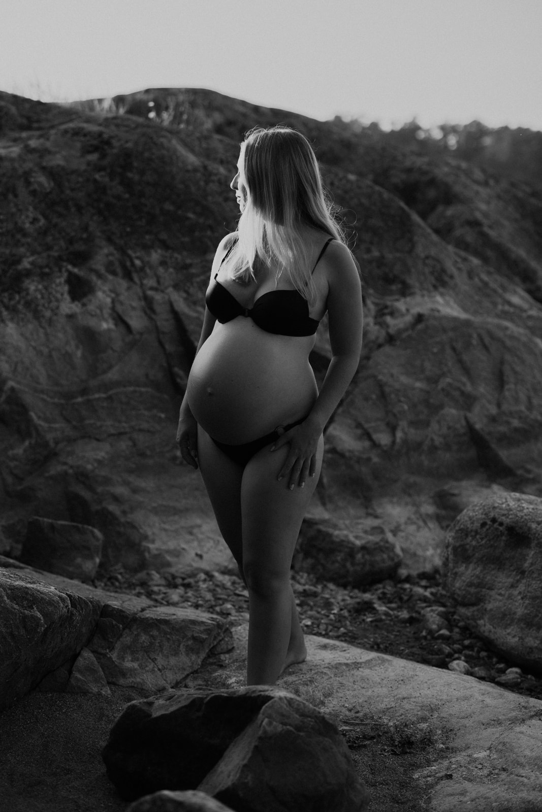 gravidfotograf stockholm gravid kvinna i bikini står bland klipporna under en gravidfotografering i stockholm