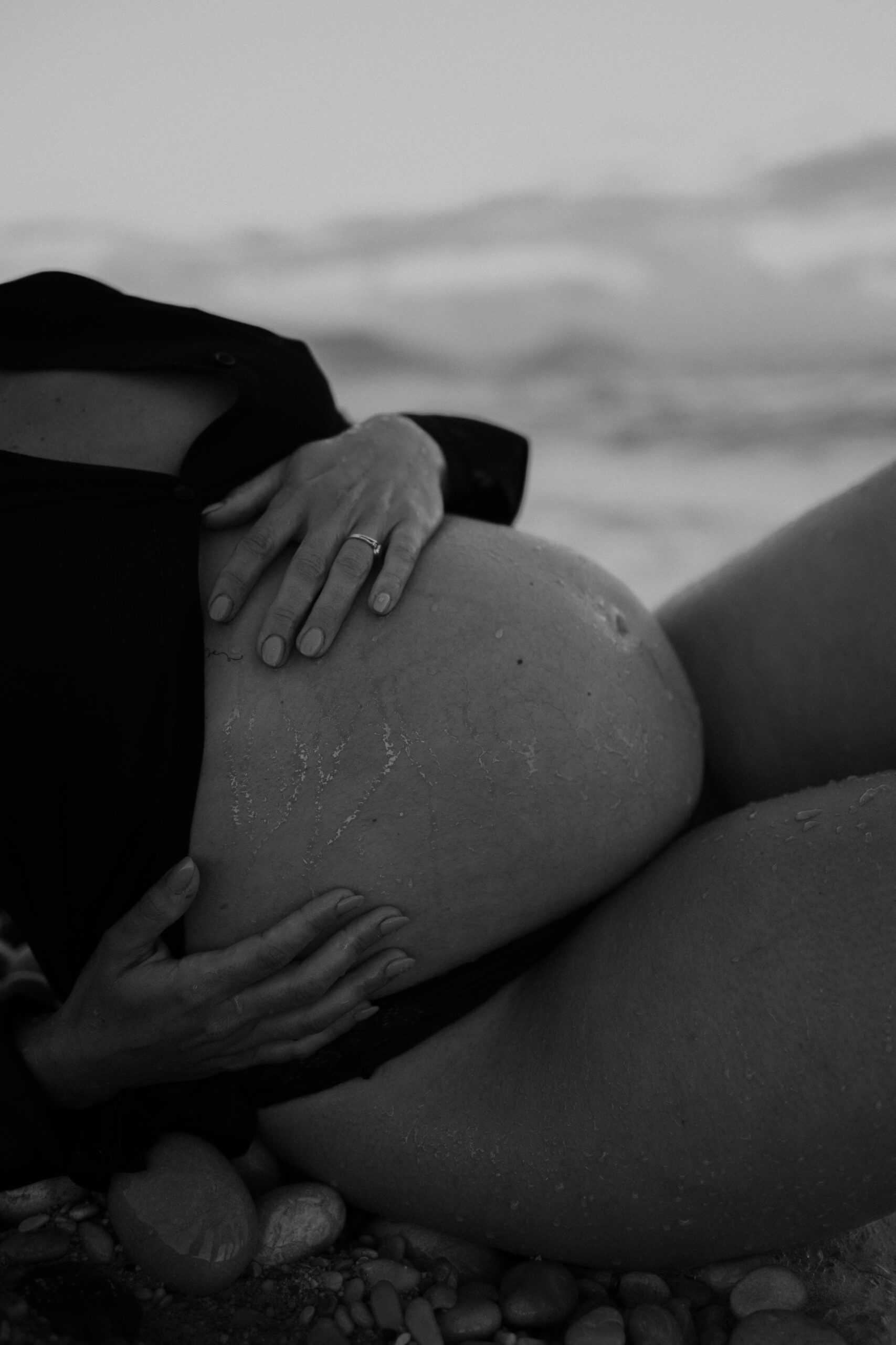 Gravid kvinna fotograferad liggande vid vatten under gravidfotografering i Stockholm