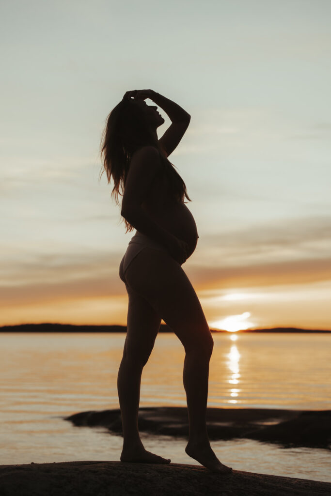 Gravid kvinna i solnedgången, silhuetten lyses upp av det varma ljuset – inspiration gravidbilder för en tidlös och harmonisk väntans stund.