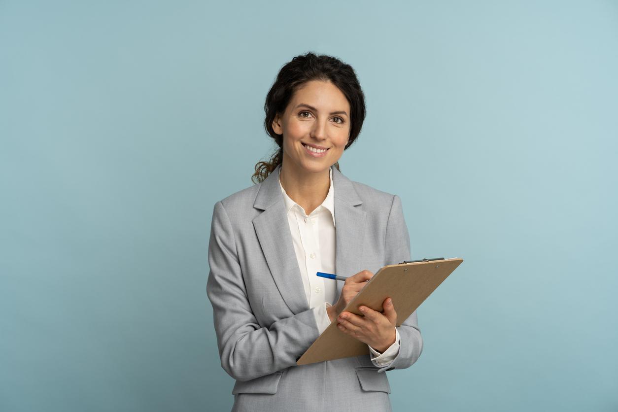 Friendly instructor or agent woman wear grey blazer and white blouse hold folder, pen looking at camera