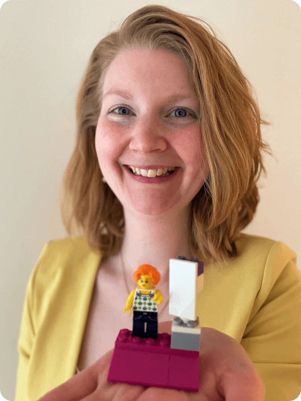 Als Karrierecoach in Hamburg bietet Ariane Mitsching Karrierecoaching in Hamburg und online an, Porträt von Ariane, die ein Legomodell in die Kamera hält.