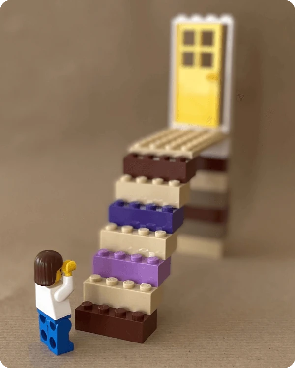 Berufliche Neuorientierung Hamburg, Startbild, Legoszene: Coachee steht verzweifelt am Fuß einer steilen Treppe, oben wartet eine leicht geöffnete Tür