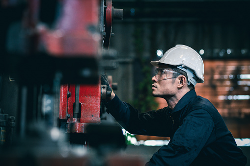 Men industrial engineer wearing a white helmet while standing in a heavy industrial factory behind. The Maintenance looking of working at industrial machinery and check security system setup in fact