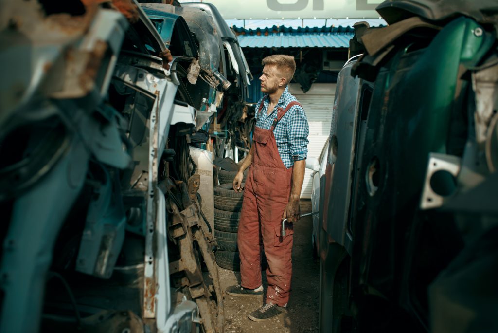 Male repairman choosing spare parts on car junkyard