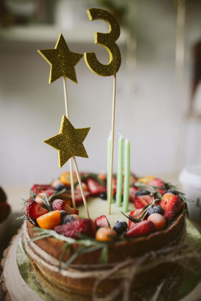 Delicious fruit-topped cake with candles and glittery number decoration, perfect for celebrations.
