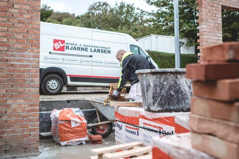 Murer 9 Murer står foran firmabil og klipper mursten til