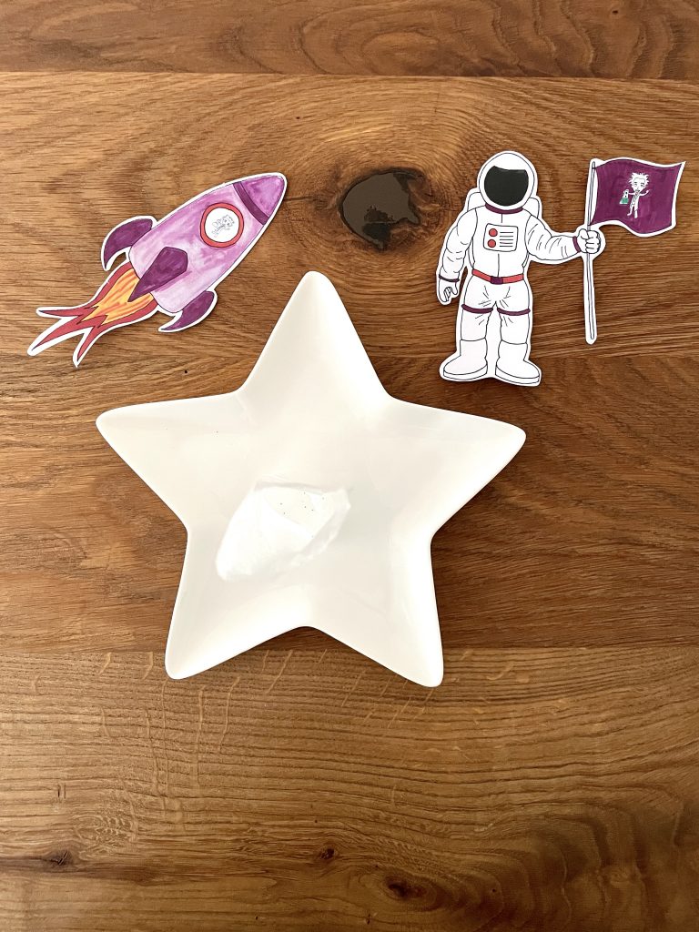 Ein Sternenteller mit aufrecht stehendem Teebeutel und einem Bild eines Astronauten sowie einer Rakete sind zu sehen.
