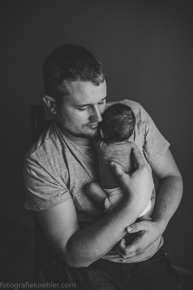 zu sehen ist ein Vater, wie er sein Baby vor der Brust hält und sanft an seinem Köpfchen riecht