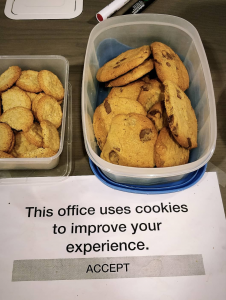 Picture of cookies in a box, below a printed sheet of paper saying "This office uses cookies to improve your experience. Accept."