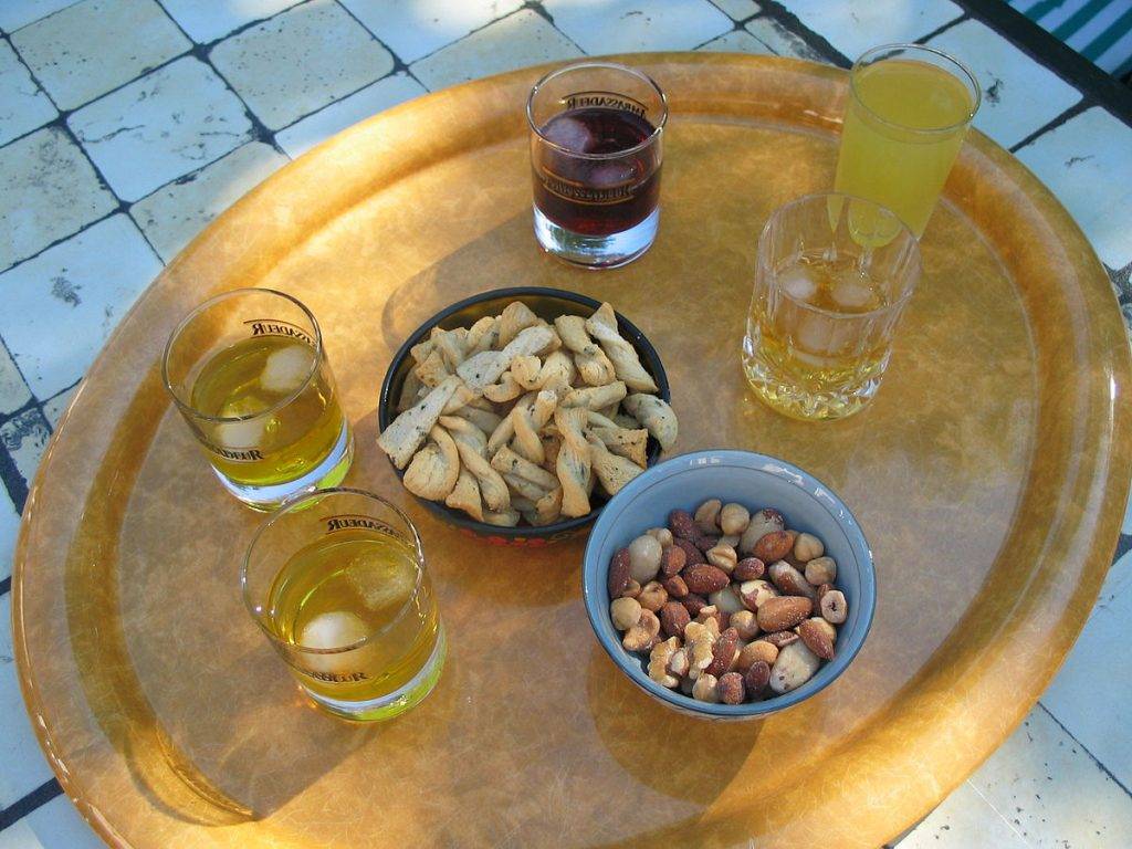 Bord utomhus med skålar med snacks och nötter samt glas med aperetif före maten eller digestif efter maten med bittra växter för matsmältningen 