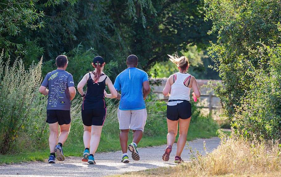 Fyra personer, två män och två kvinnor joggar tillsammans i naturen med linne och shorts en solig varm dag