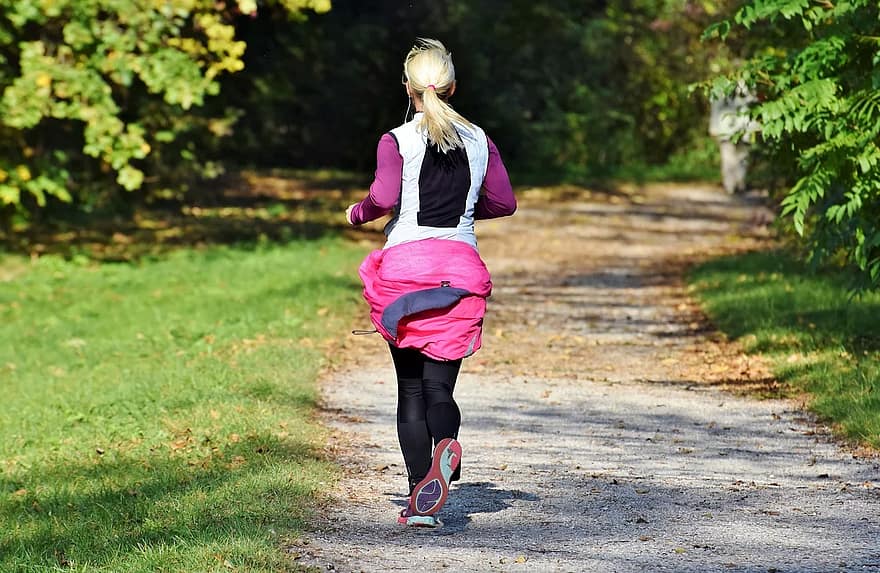 blond kvinna i träningskläder och jacka runt midjan springer på grusväg i en park, fysisk aktivitet ger starkt skelett mer än att pH-värdet urholkar skelettet genom kosten. Påverka ph-värde med kosten och fysisk aktivitet