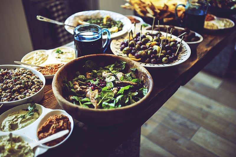 Buffe med hälsosam mat i olika skålar och på tallrikar på ett träbord, oliver, grönsaker, bönor