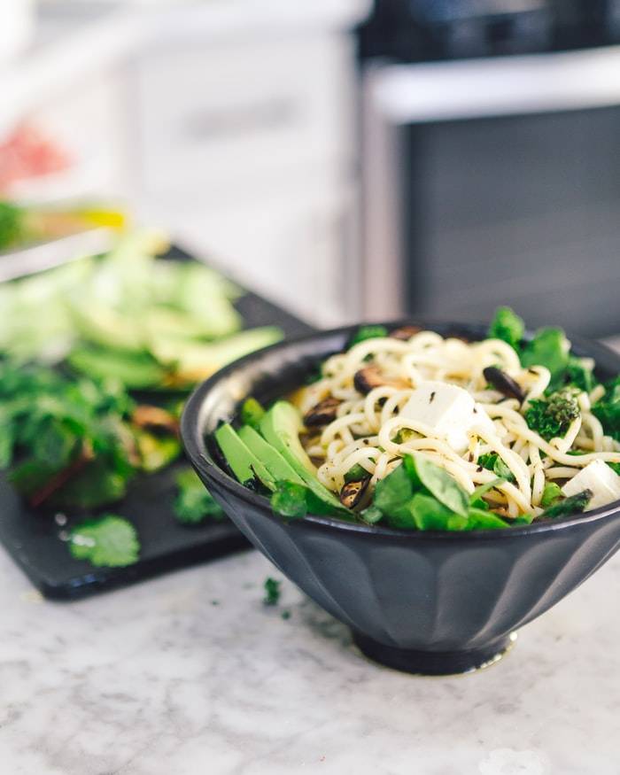 Svarta skålar med asiatisk mat med tofu soja, grönsaker och nudlar, skärbärda i bakgrunden, fytoöstrogen mat