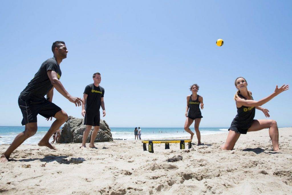 kvinnor och män spelar boll på strand i solen