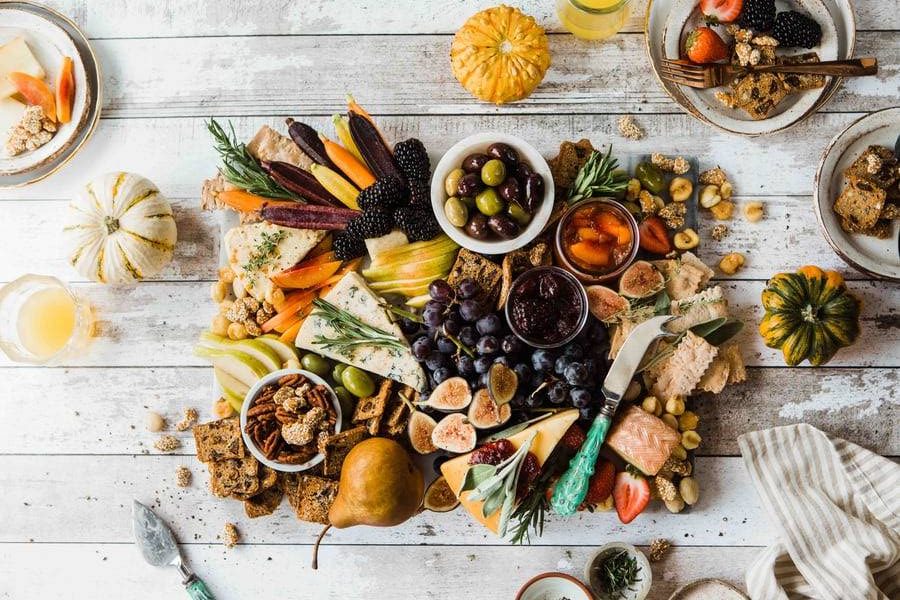 näringsrik mat, grönsaker, nötter, ostar och frukter på bräda på vitt bord med skålar av snacks, varierad näringsrik kost som positivt påverkar immunförsvaret