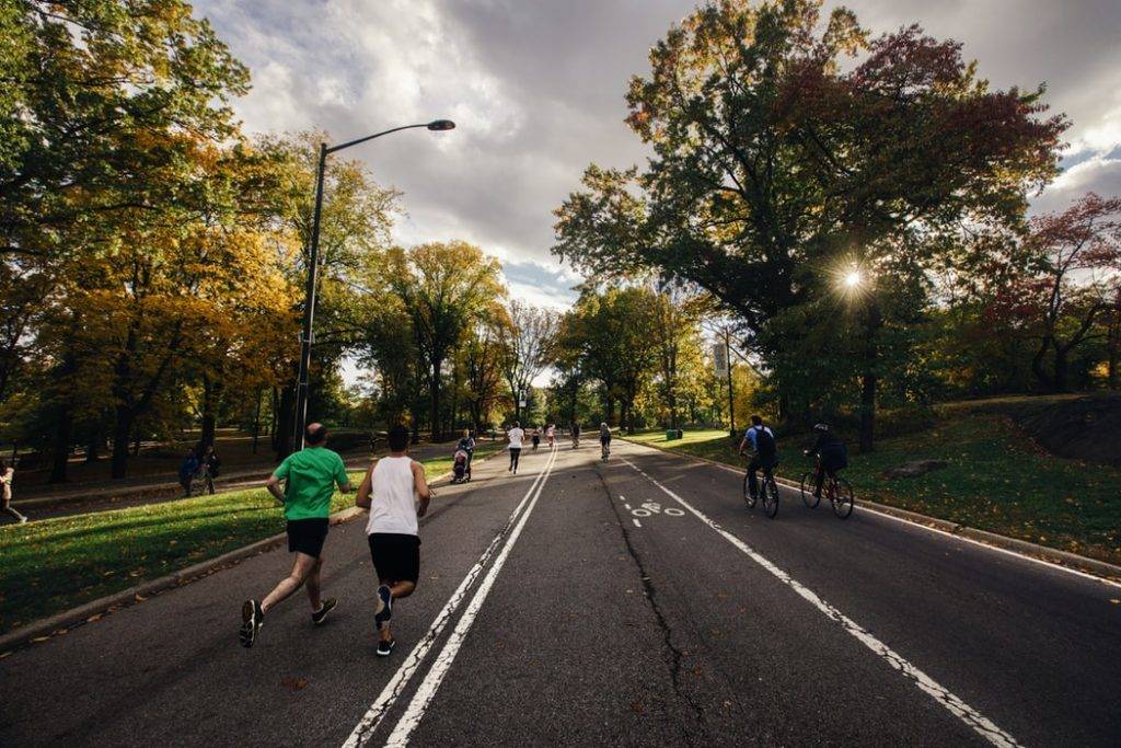 människor springer, cyklar och promenerar en varm solig dag utomhus på asfalterad gång och cykelväg med träd och buskar vid sidan. Fysisk aktivitet påverkar immunförsvaret positivt