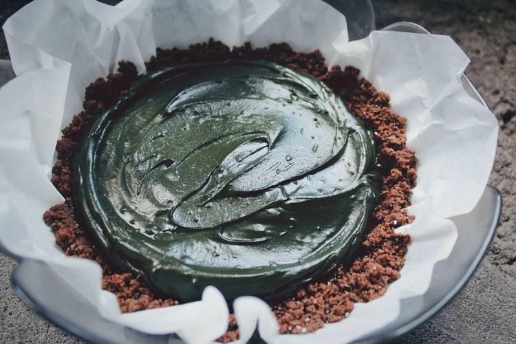 kaka gjord med frosting med spirulina. Frostingen och krämen ovanpå den bruna kakan är mörkt grön av spirulinapulvret. Kakan ligger på ett bakplåtspapper på en tallrik