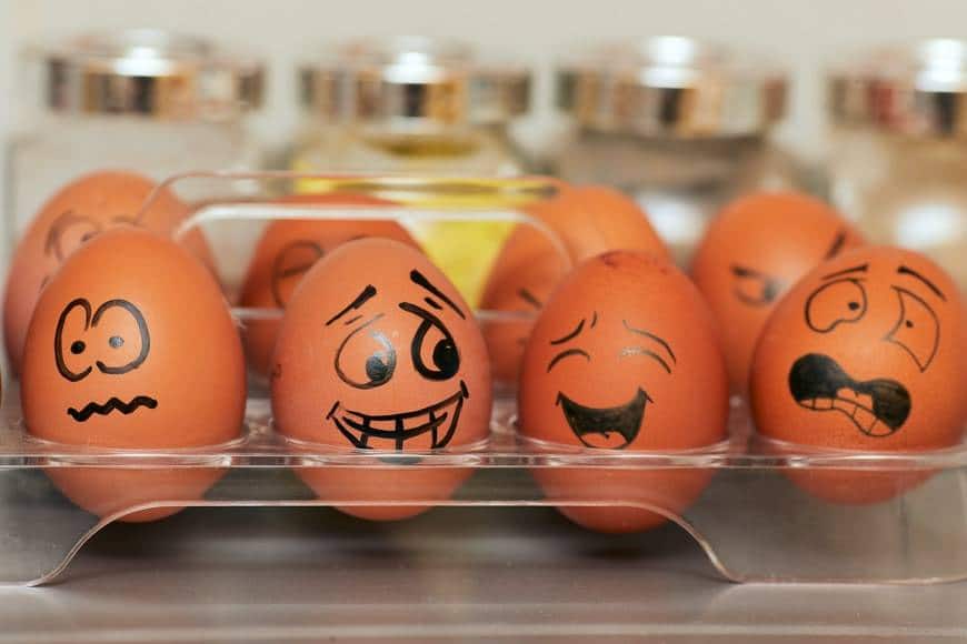 Bruna ägg målade med svart penna i olika känslouttryck. Ilska, ängslan, glädje, rädsla, skratt, gråt. Äggen står i en plasthållare för ägg med glasburkar i bakgrunden. Sömnbrist leder till svårigheter att styra känslorna.