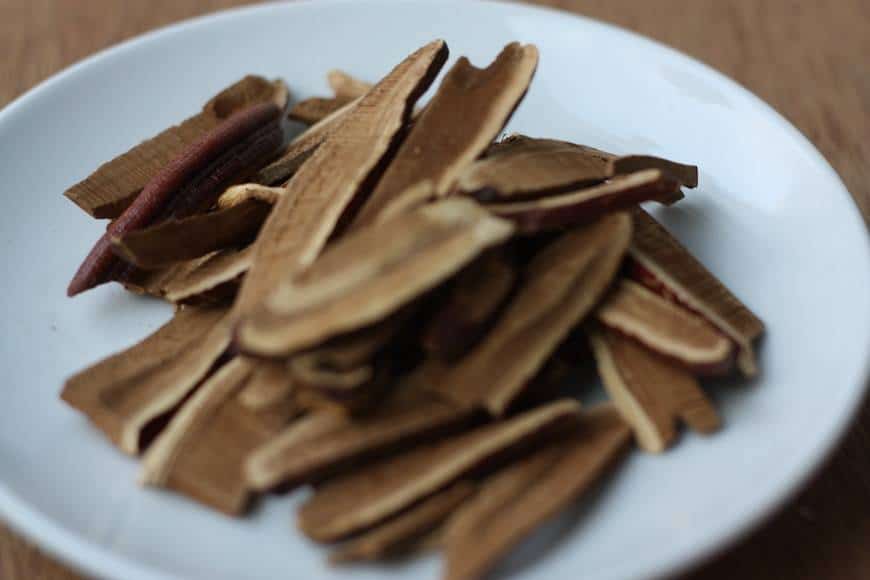 Reishi svamp, torkad och skivad i bitar. Reishisvampen ligger på en vit tallrik som står på ett träbord. Medicinalsvamp