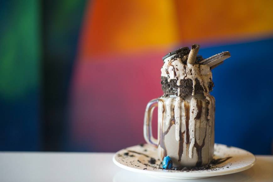 Krämig chokladdrink med grädde och oreo på toppen. Chokladdrinken är upphälld i ett glas med handtag och står på en vit tallrik med chokladsås på. På insidan av drinken rinner mörkchokladsås nerför sidorna och ovanpå ligger skopor med glass och grädde. Kex är nedstoppade i drinken och glassen. Längst upp ligger en kaka oreo. Mejeriprodukter