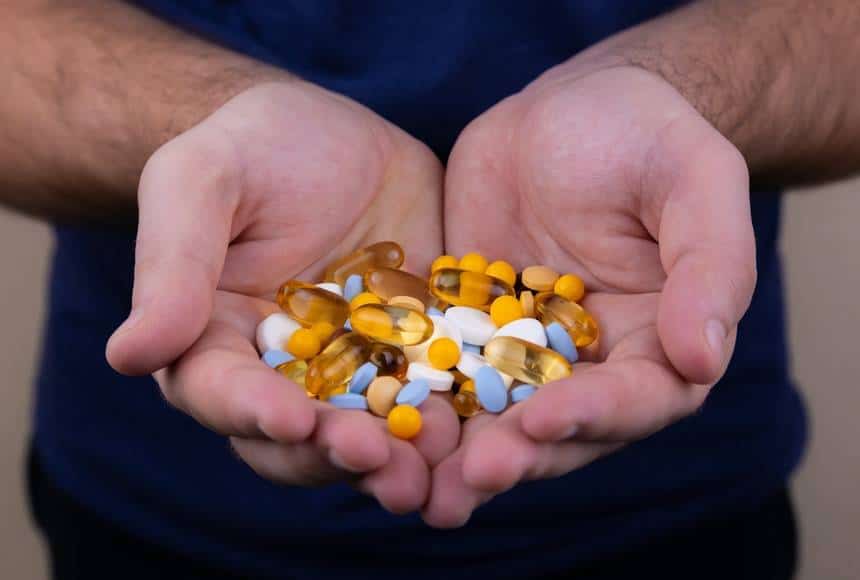 Man håller kosttillskott i form av piller och kapslar i sina händer. Bilden är tagen enbart på mannens utsträckta händer som är full med piller och tabletter i många olika former och färger.