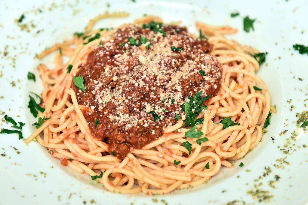 Spagetti och köttfärssås på en bit tallrik med persilja stött ovanpå. Bilden är i närbild på maten där spagettin ligger i botten och köttfärsåsen i mitten ovanpå. Kolhydrater ansamlar vätska