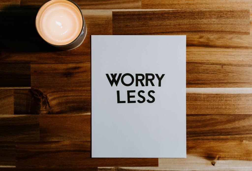 Vitt papper på träbord med orden "Worry less" - oroa dig mindre. Bredvid lappen står ett tänkt värmeljus. Gå ner i vikt vid stress är svårt