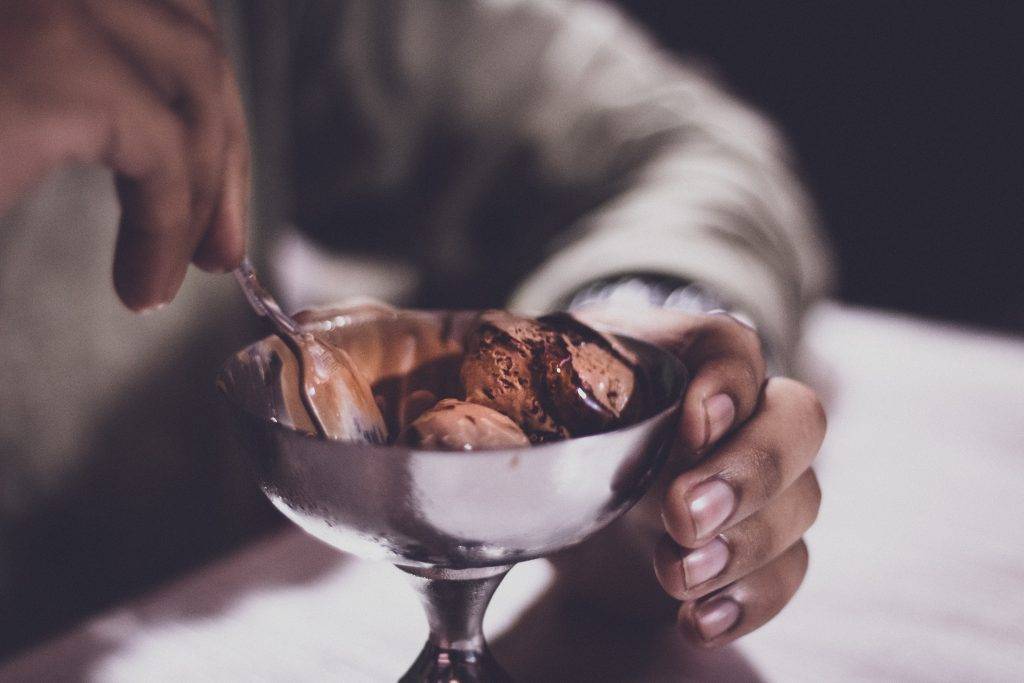 Kvinnas händer håller kring en lite skål i rostfritt stål med chokladglass. Bilden är tagen i närbild på skålen och händerna. choklad