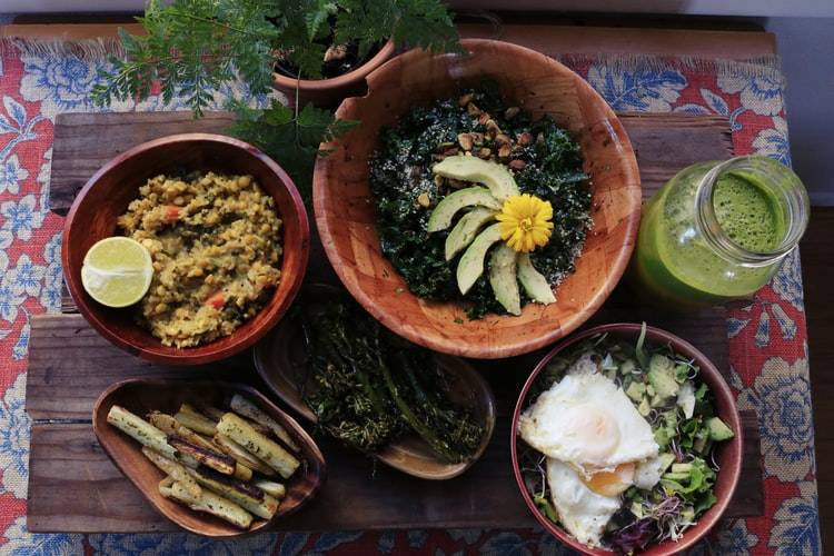 Tallrikar med hälsosam mat påp bord. Sallad med ägg, sjögrässallad, bönor, nyttig mat. Bredvid en glasflaska med en grön smoothie eller grön juice.