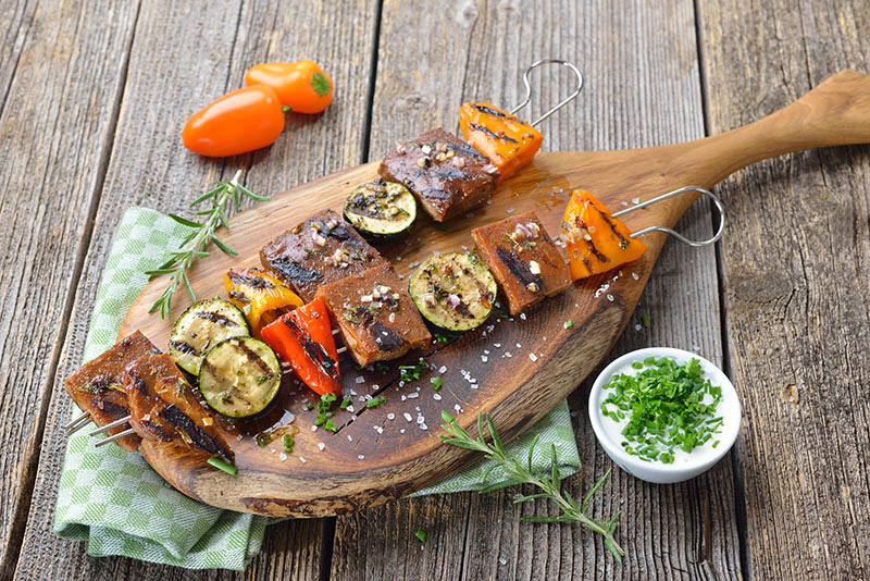 Grillad tofu på grillspett med grönsaker på skärbräda med tzatziki i en liten skål bredvid