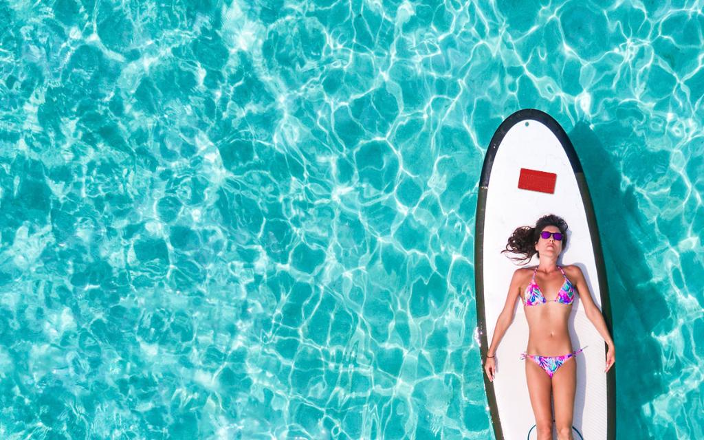 Woman in bikini lying on paddleboard in water. Above her head is a red keyboard.