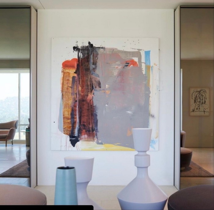 A modern interior with a large abstract painting on a white wall, two tall sculptural vases in the foreground, mirrored panels, and a seating area in the background