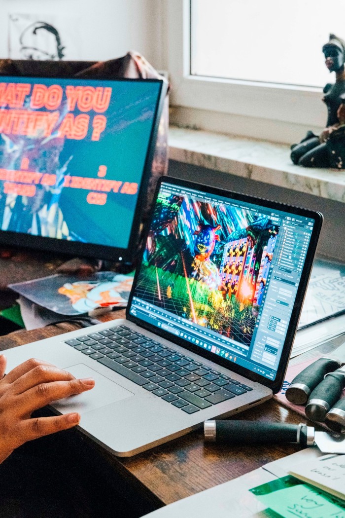 A computer and a laptop are open on a desktop, one displaying the starting instructions for a video game that reads “what do you identify as?” over three options, the other screen containing in-play graphics for a game 