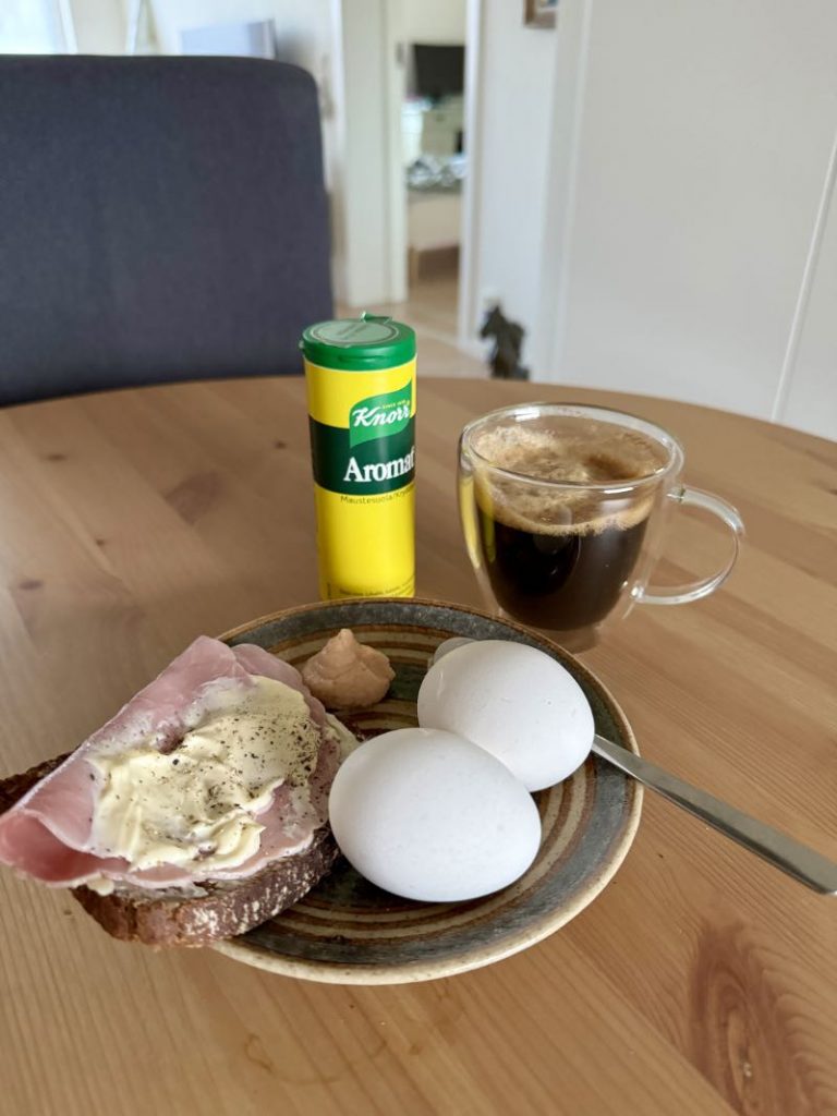 Frukost på ett bord. Skinkmacka och 2 ägg och kaffe.